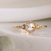 A 14k yellow gold ring featuring a rose cut diamond centerpiece with smaller accent diamonds, displayed on a white marble surface.