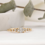 Gold ring with a diamond on a white surface with green leaves in the background