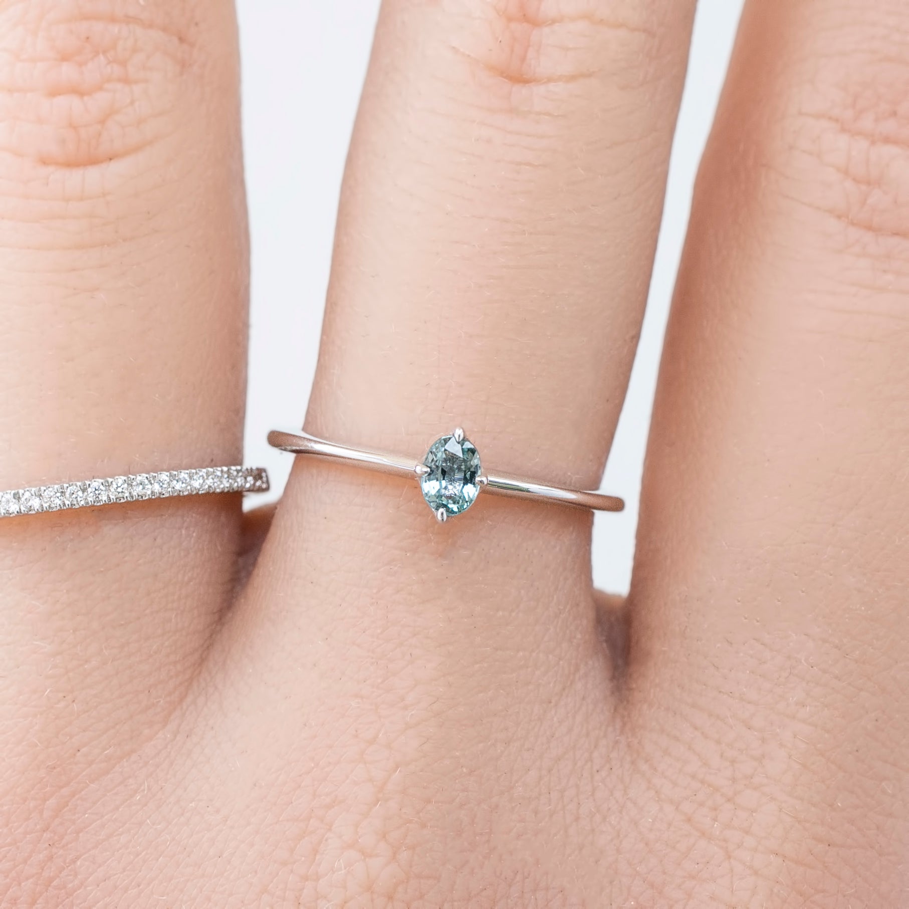 Close-up of a natural blue-green oval sapphire showing the unique unheated color and white gold prongs on a hand