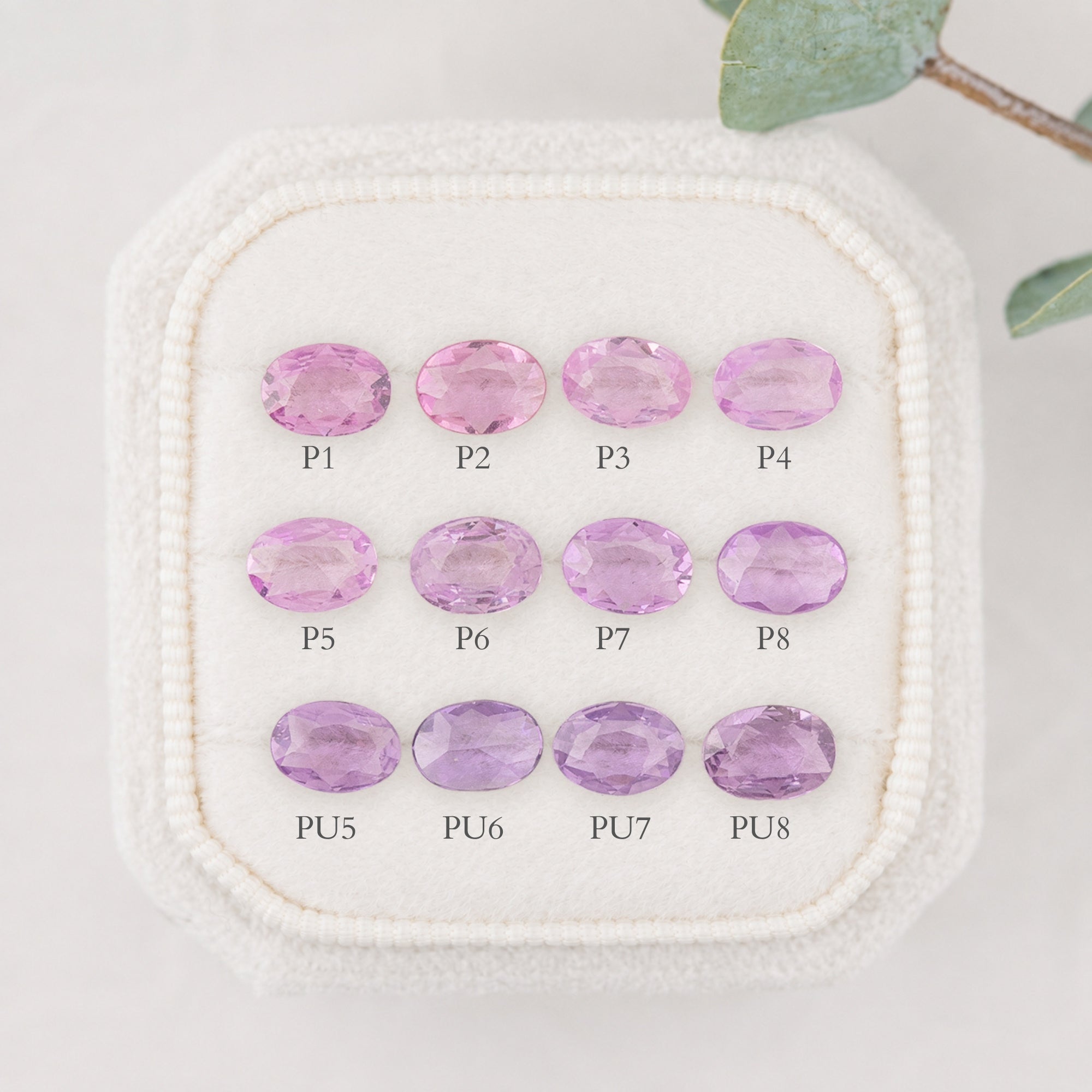 Nine oval-cut pink and purple gemstones arranged in a 3-by-3 grid on a white textured display pad, with labels P1 through PU8 beneath each stone.