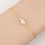 Gold bracelet with a central gemstone on a wrist against a neutral background