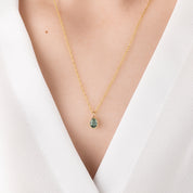 Gold necklace with a green pendant on a white background