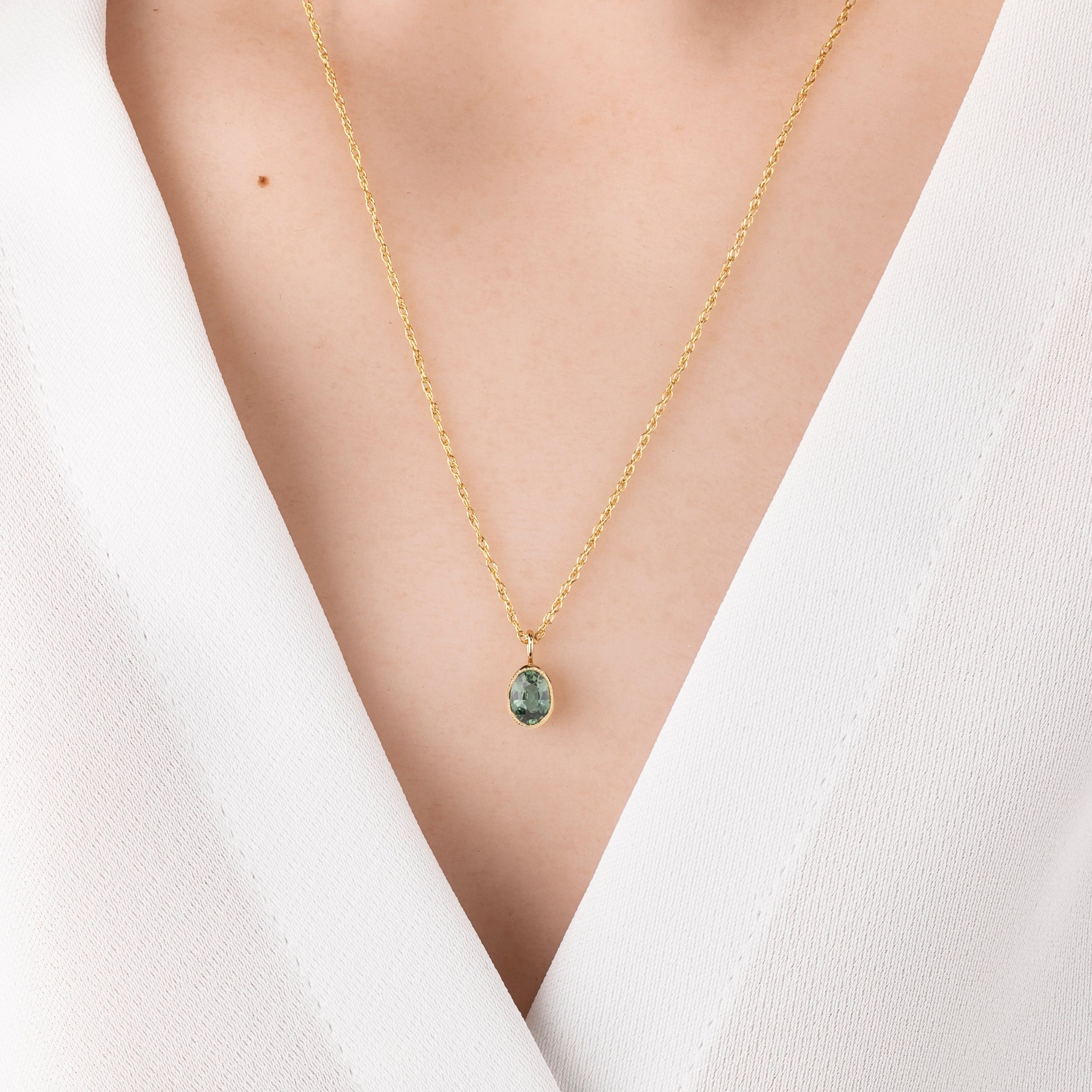 Gold necklace with a green pendant on a white background