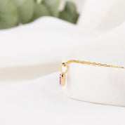 Gold necklace with a purple gemstone pendant on a white surface.