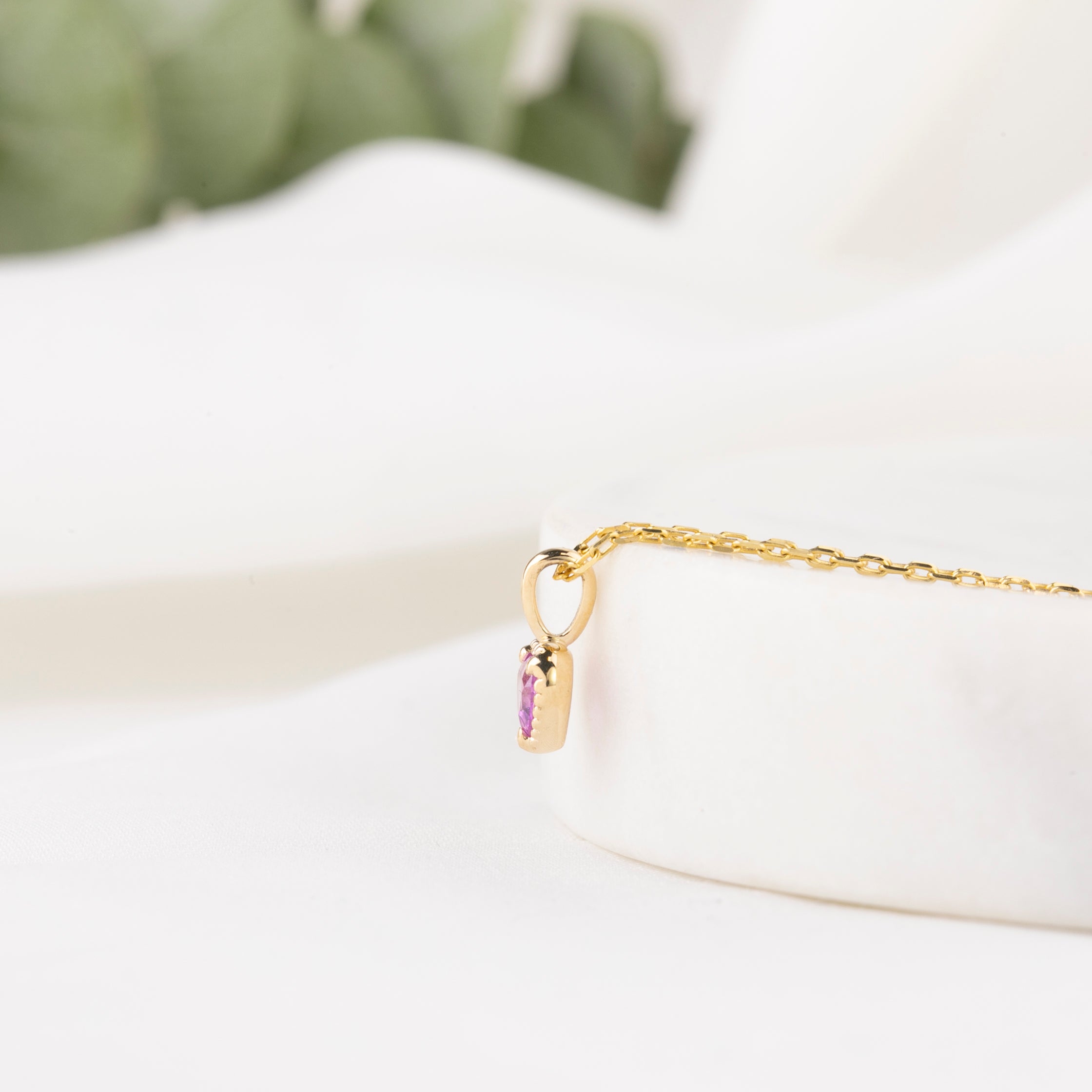 Gold necklace with a purple gemstone pendant on a white surface.