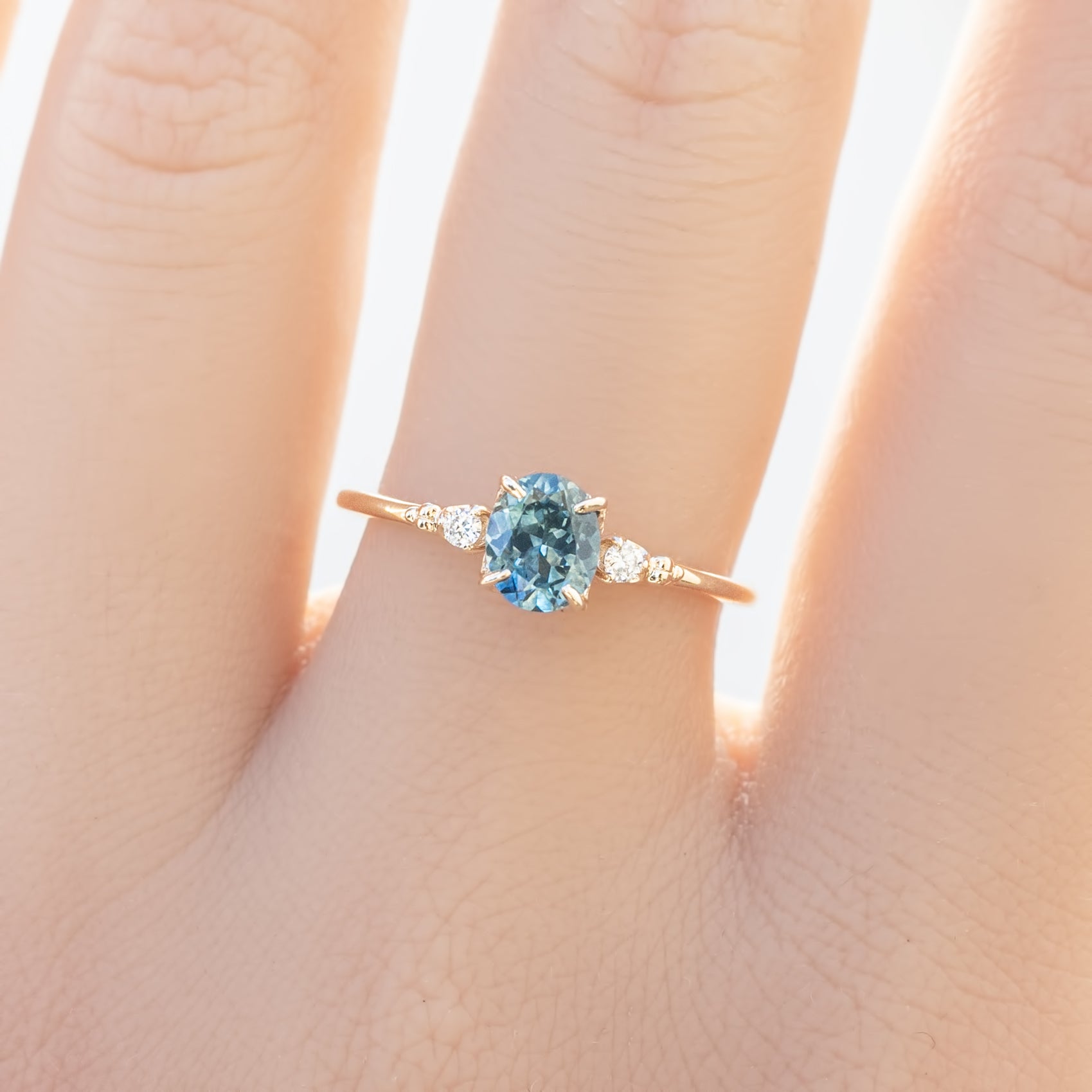 Estel Ring featuring an oval 0.85ct oval teal Montana sapphire with natural diamond accents in 14k yellow gold on the finger