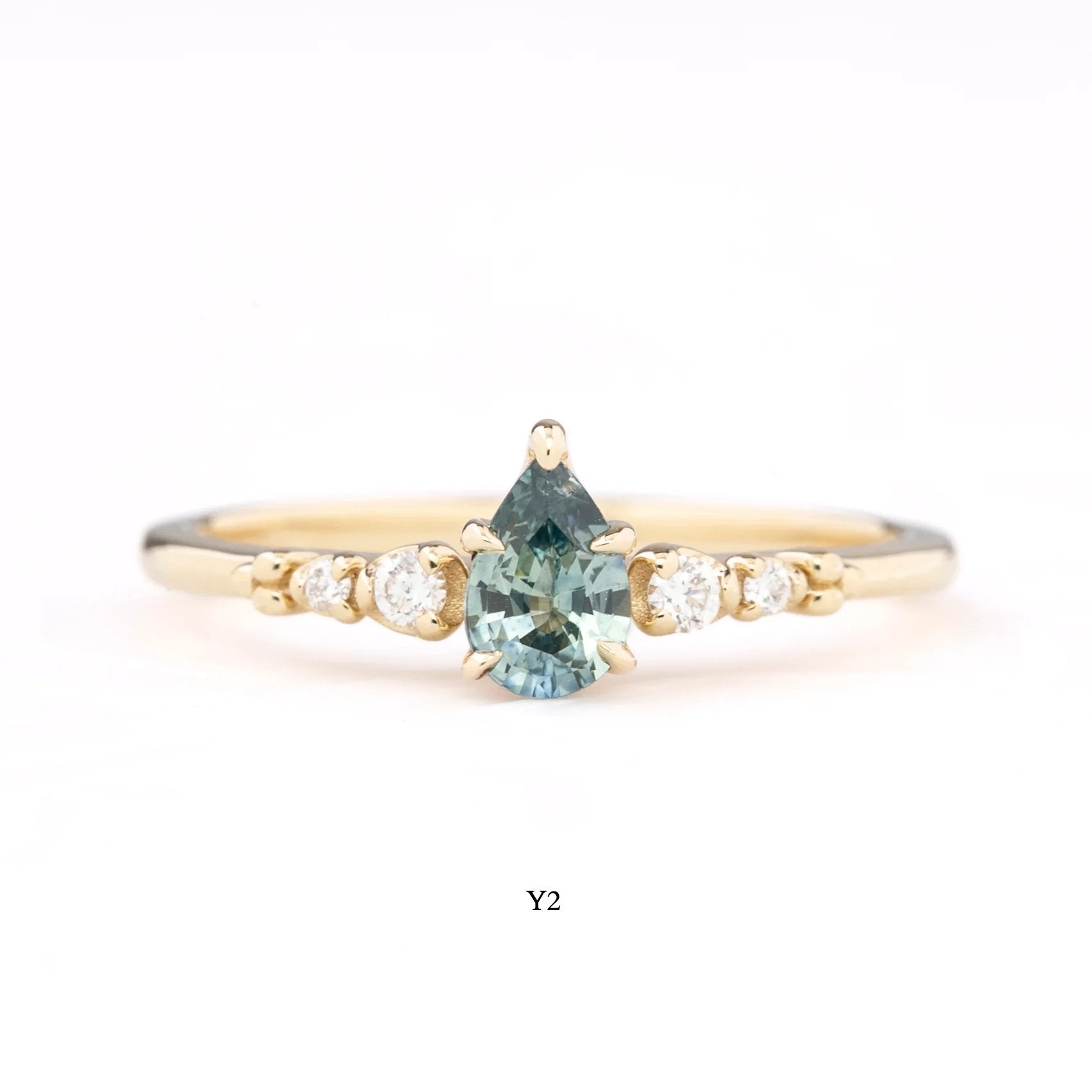 A collection of rings with pear-cut Montana sapphires in various colors, set in 14k gold with accent diamonds, displayed on a white surface.