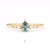 A collection of rings with pear-cut Montana sapphires in various colors, set in 14k gold with accent diamonds, displayed on a white surface.