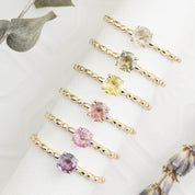 Gold rings, each featuring a different color of sapphire gemstone set in 14k gold solitaire style.