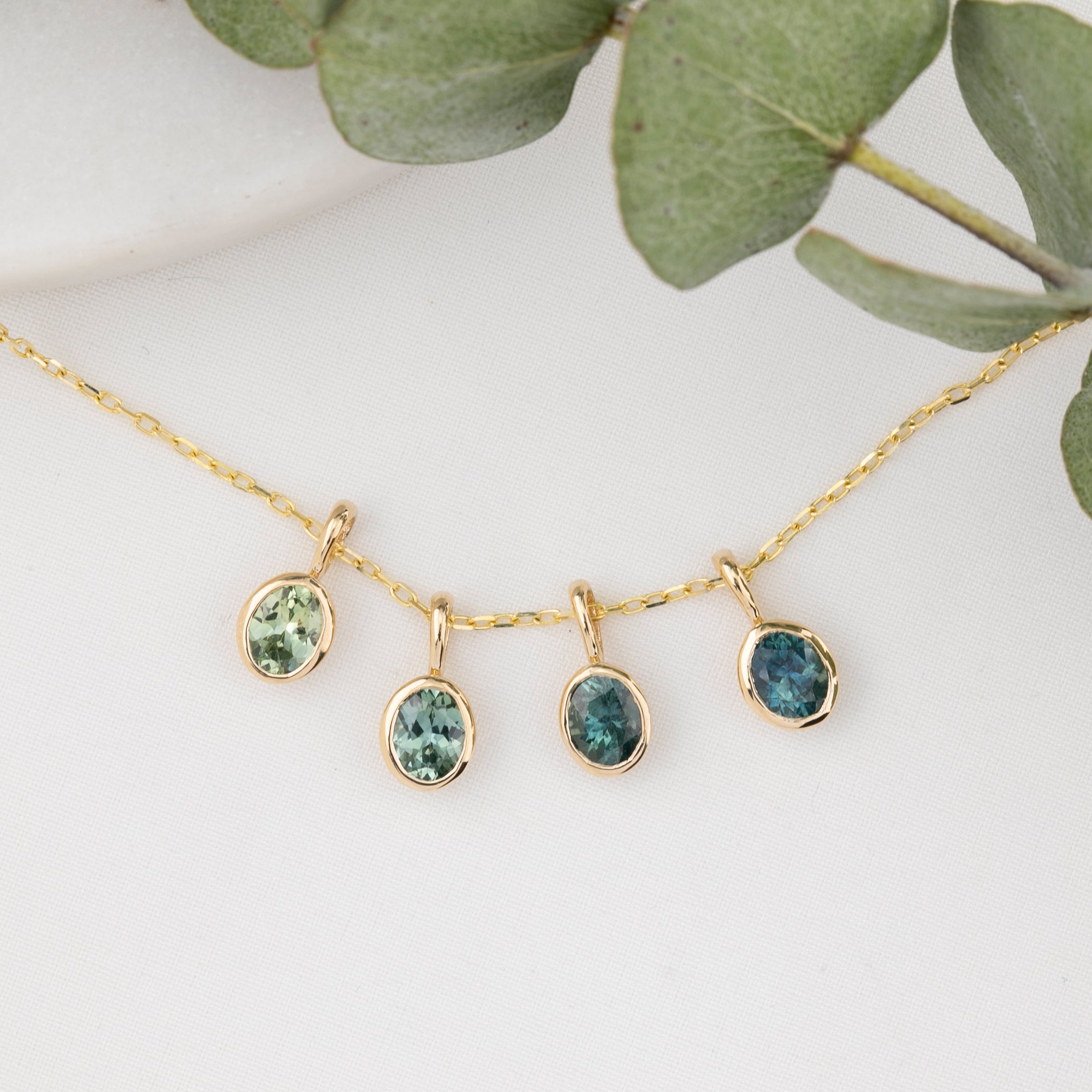 Gold necklace with four green gemstone pendants on a white background with eucalyptus leaves.