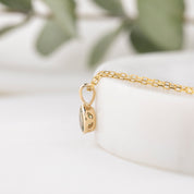 Gold necklace with a pendant on a white surface with green leaves in the background
