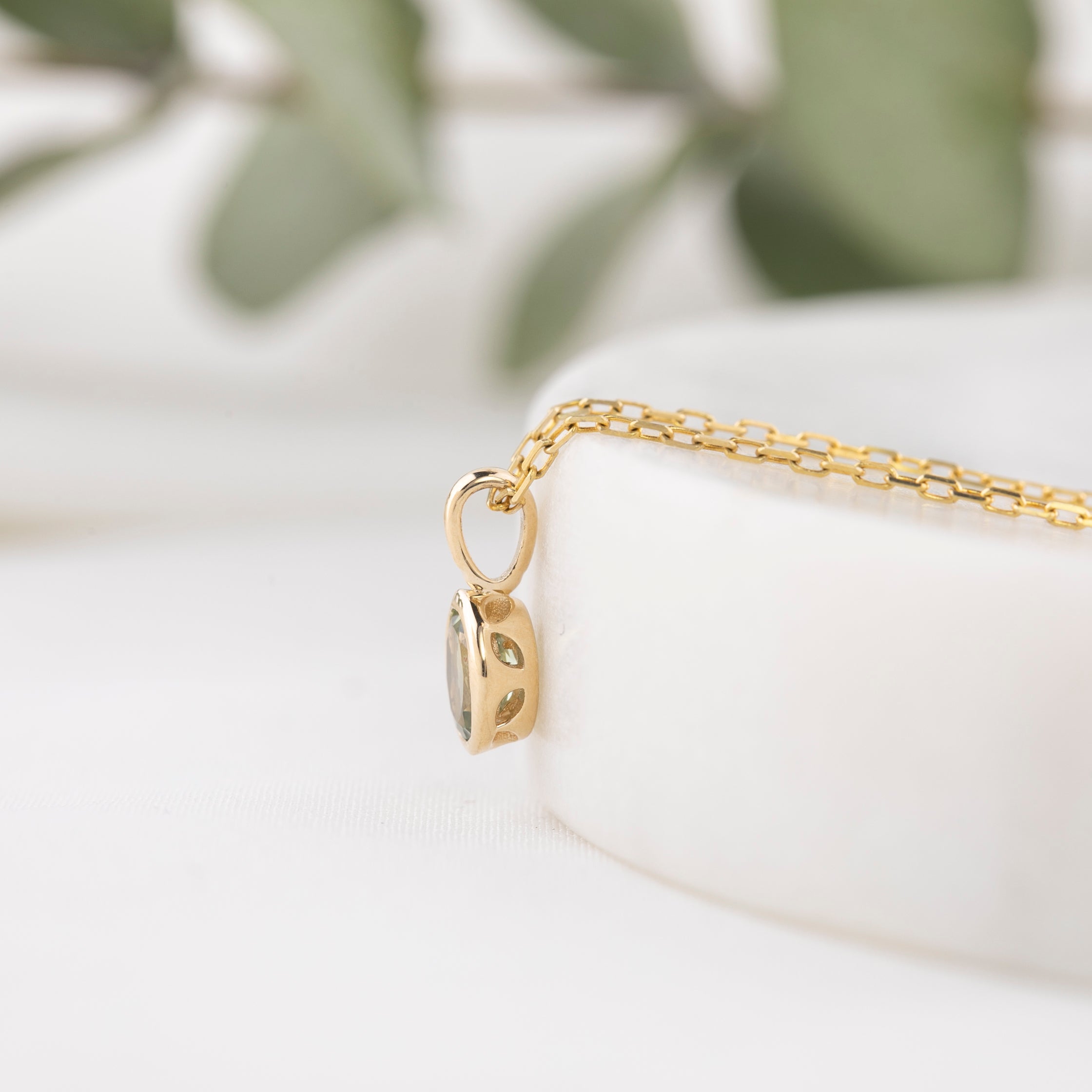 Gold necklace with a pendant on a white surface with green leaves in the background