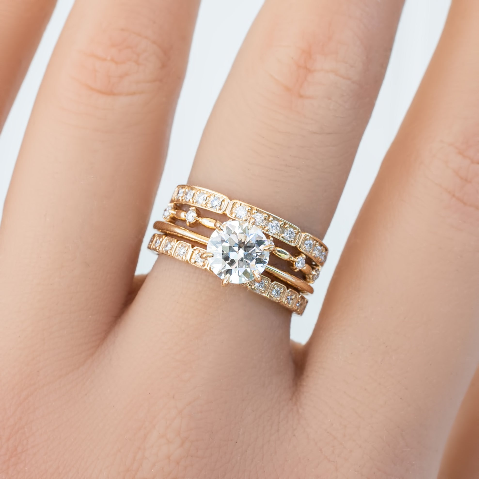 Close-up of a hand wearing a Distant Star Ring with natural white diamonds and solid gold band on a light background