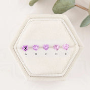 Five heart-shaped pink gemstones on a hexagonal white stone with a blurred green plant in the background.