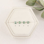 Set of green heart-shaped earrings on a white hexagonal stand with leaves in the background