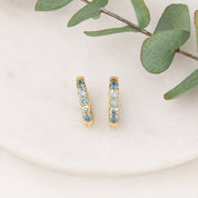 Gold hoop earrings with gemstones on a white plate with green leaves.
