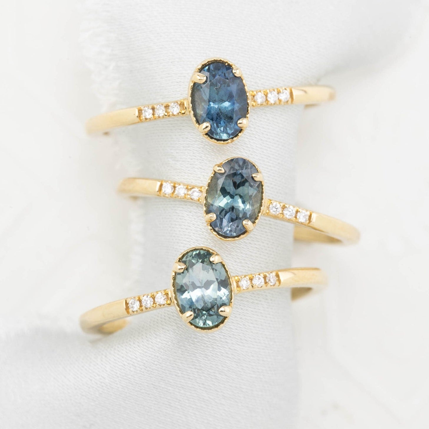 Three Grace rings eaturing a 0.60ct oval blue-green Montana sapphire and a 14k gold pave diamond band.