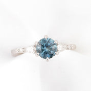Estel Fleur round engagement ring featuring a 1.34ct round blue Montana sapphire in a 14k white gold floral setting.