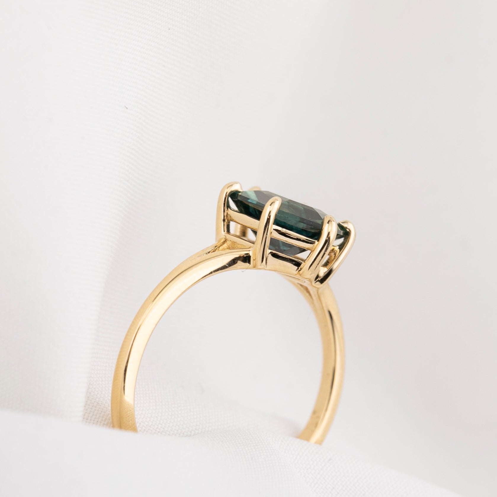 side view of Gold ring with a green gemstone on a white background
