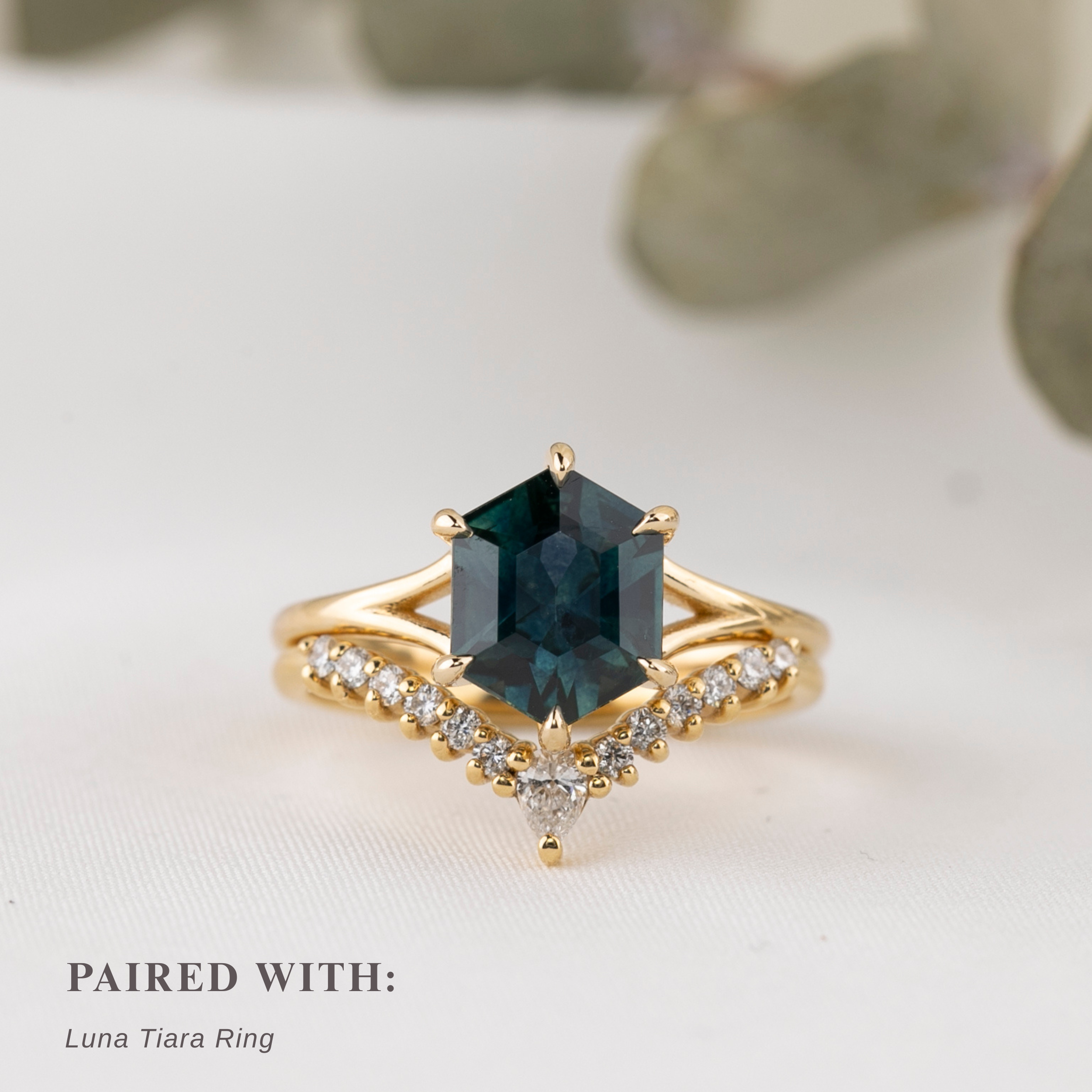 Gold ring with a hexagon shape green gemstone on a light background stacked with diamond curved ring