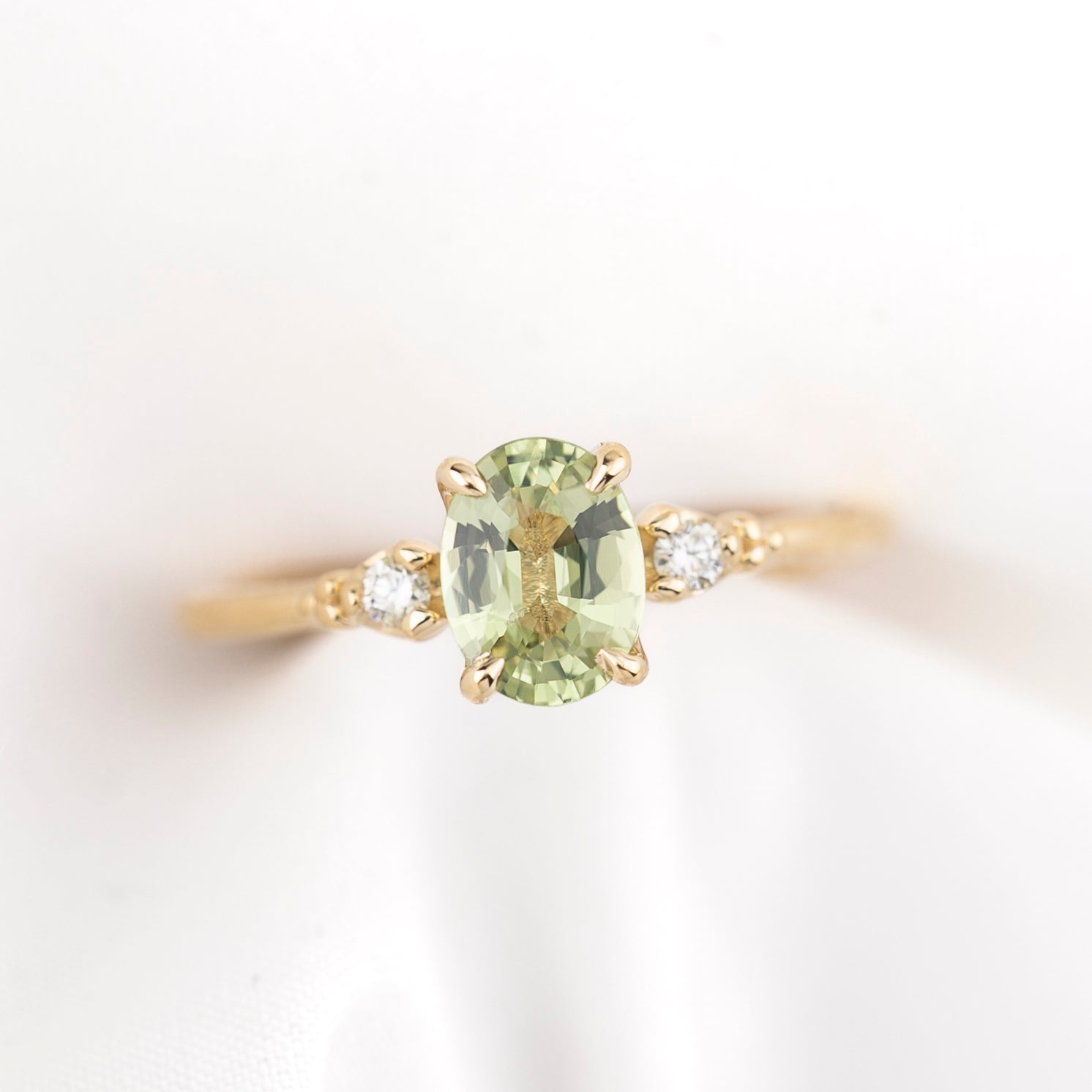 Gold ring with an oval green sapphire with two accent diamonds on a light background