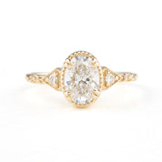 A golden ring featuring a central oval-shaped brilliant cut diamond with six smaller accent diamonds around it, set in a low-profile four double claw prong setting.