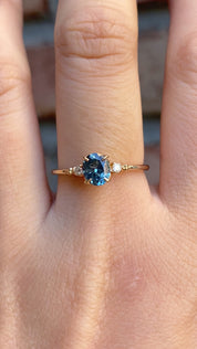 Estel Ring featuring an oval 0.85ct oval teal Montana sapphire with natural diamond accents in 14k yellow gold on the finger