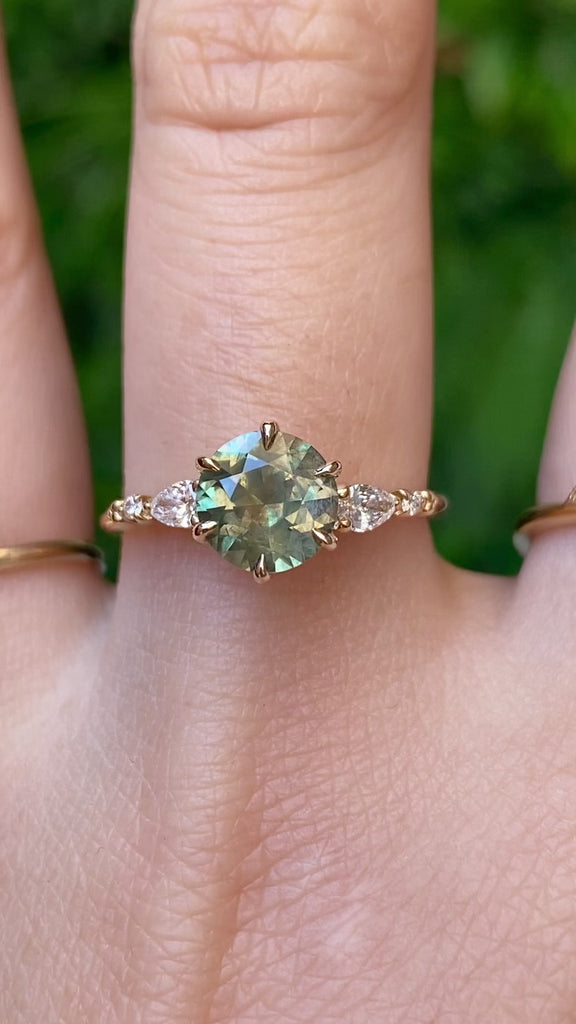 Video of Estel Fleur Petal Ring with a 1.53ct round green Montana sapphire and diamond accents in 14k yellow gold on a finger.