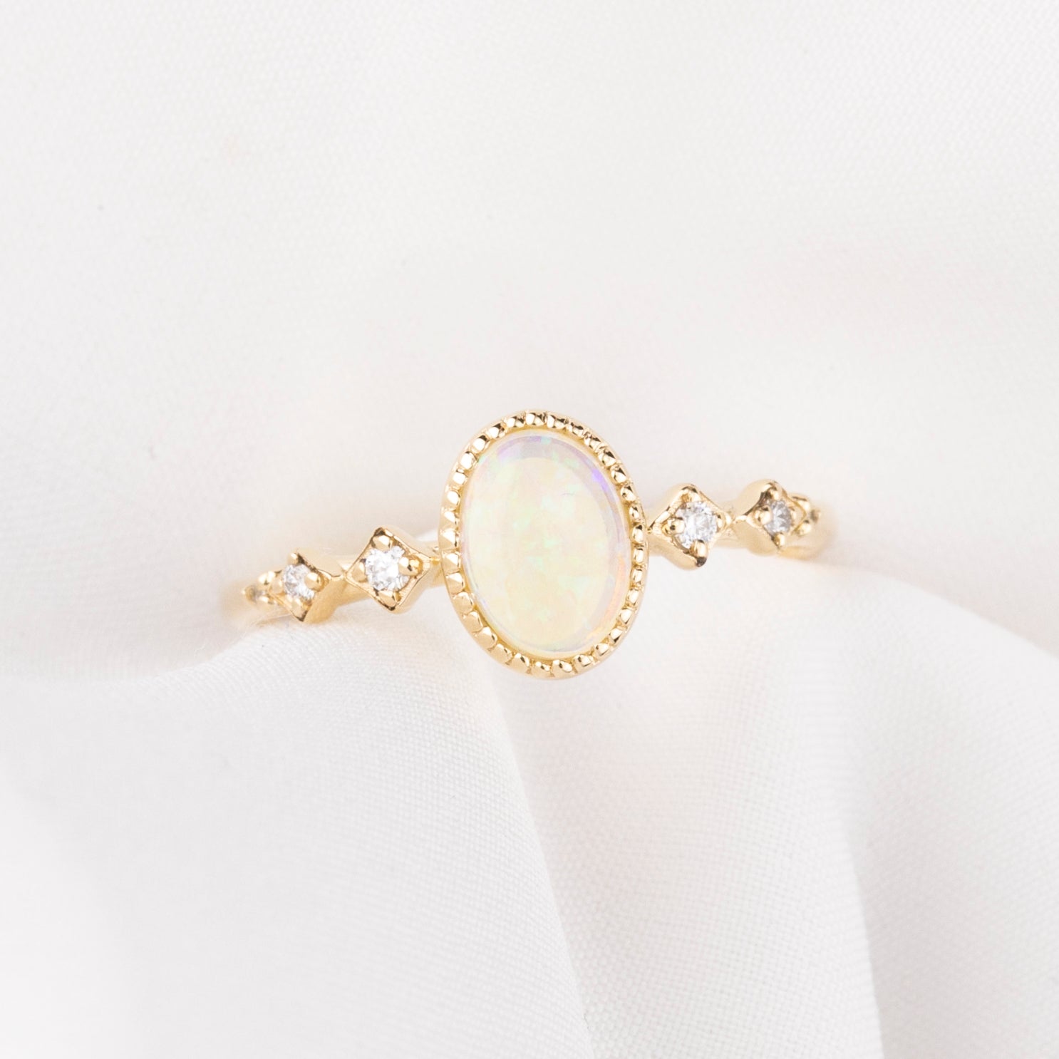 Gold ring with a central opal stone and smaller diamonds on a white background