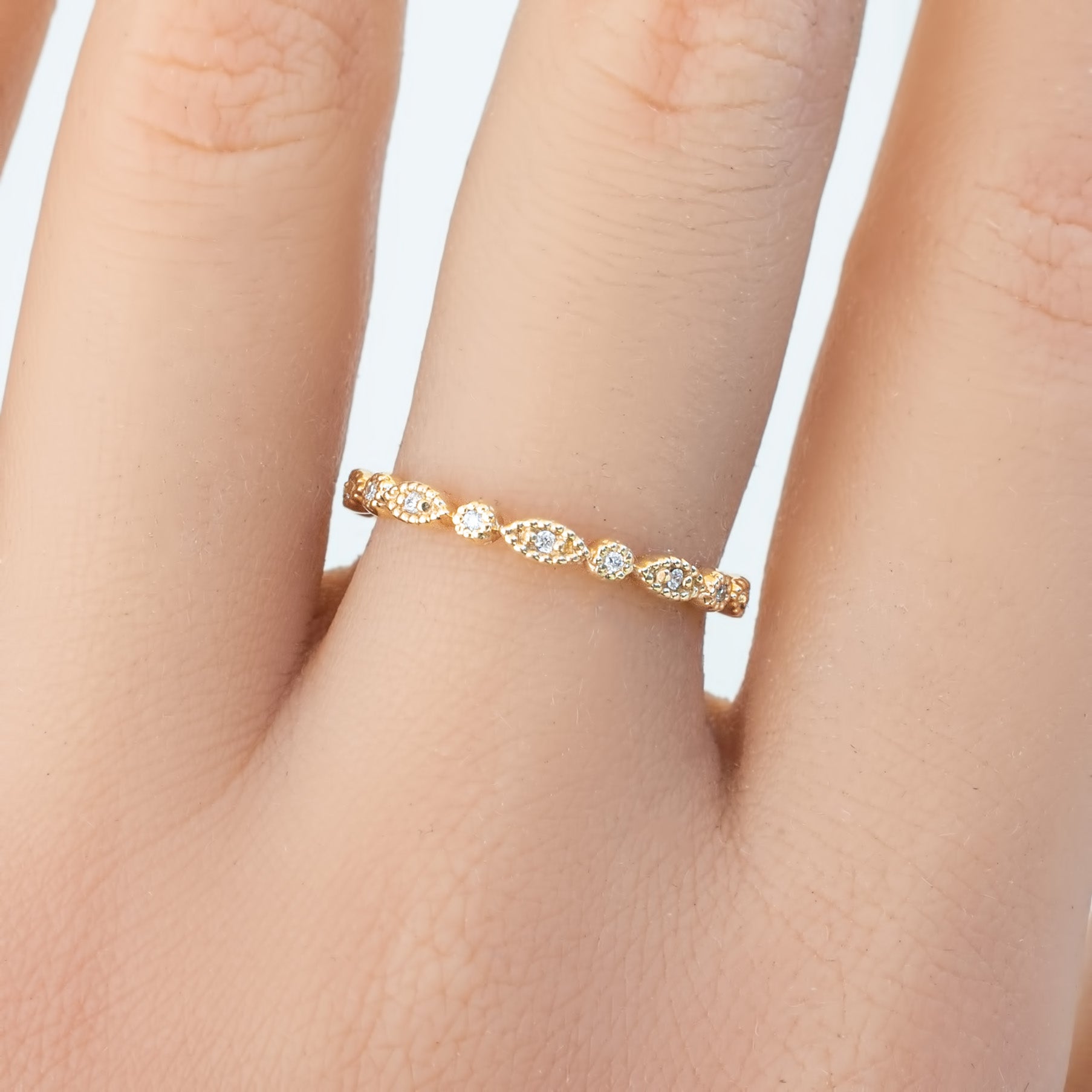 Gold petite eternity ring with delicate milgrain and natural white diamonds on a model's finger
