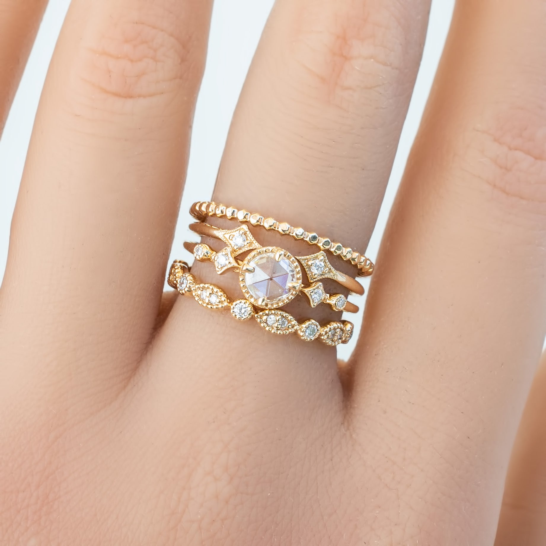 Close-up of a hand wearing three gold rings with diamonds, highlighting the bead eternity ring style band.