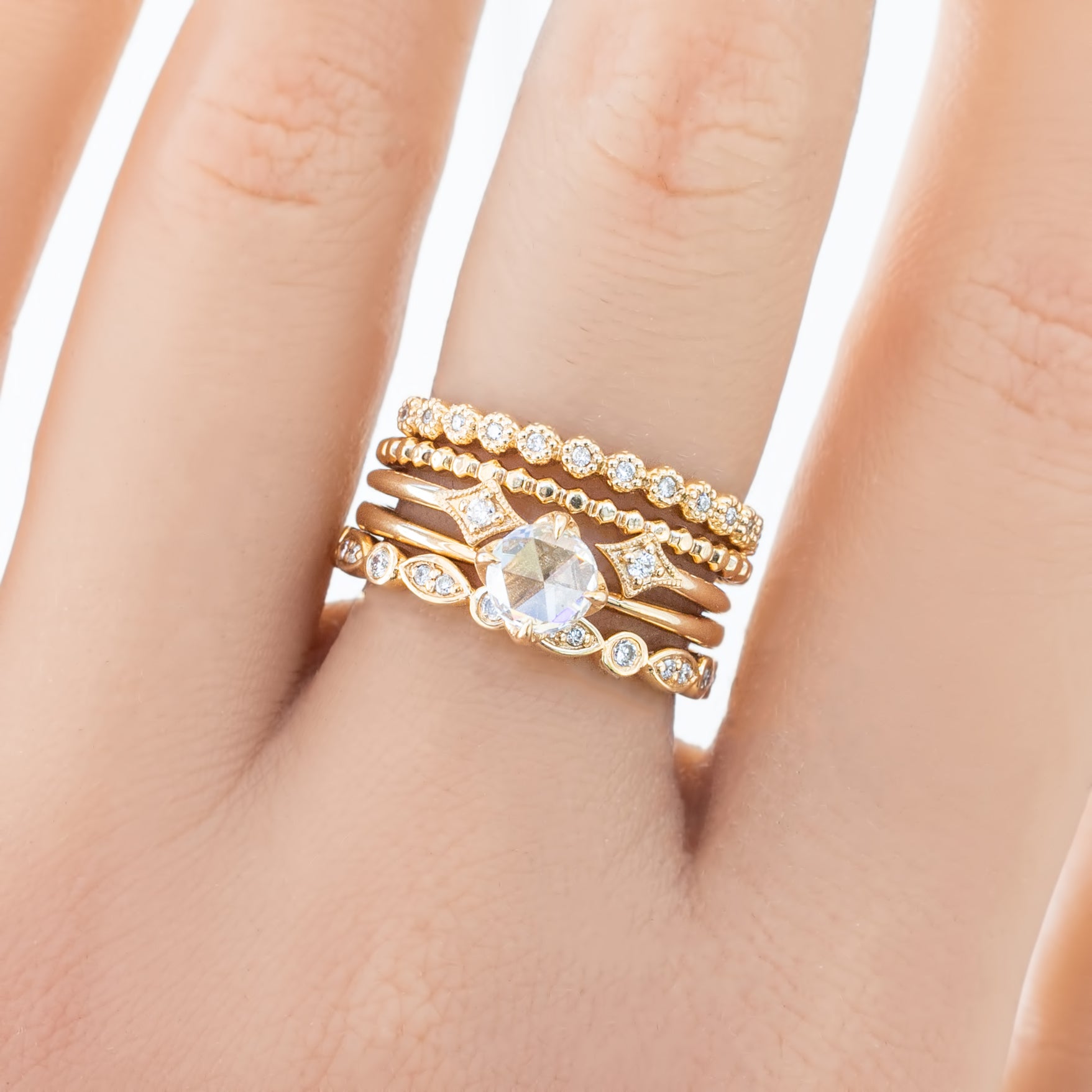 Close-up of a hand wearing multiple gold rings including a Bead Eternity Ring with small round beads and diamonds