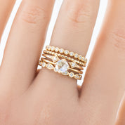 Close-up of a hand wearing multiple gold rings including a Bead Eternity Ring with small round beads and diamonds