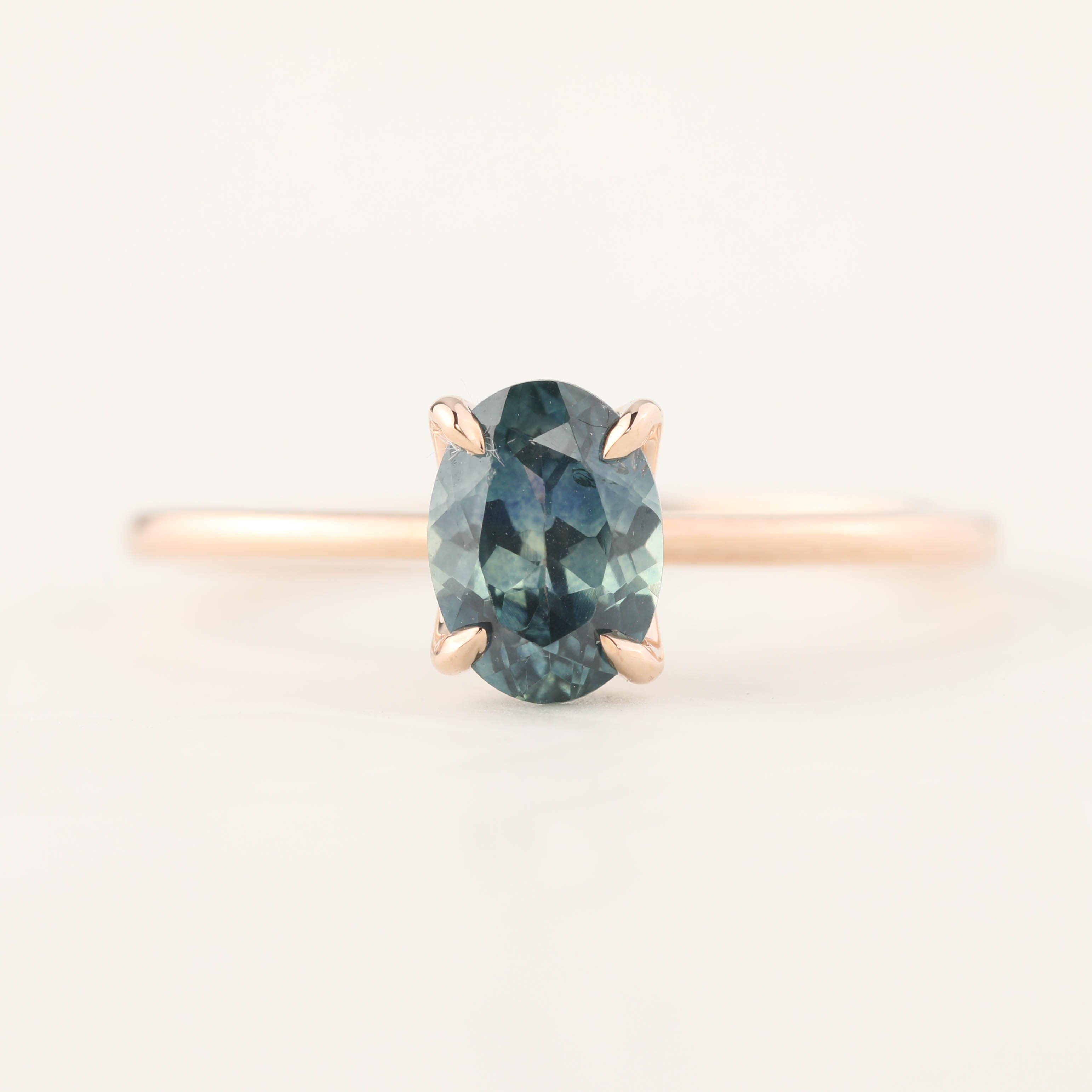 Delicate rose gold ring with a 1.00ct oval teal blue Montana sapphire in a high profile flower setting