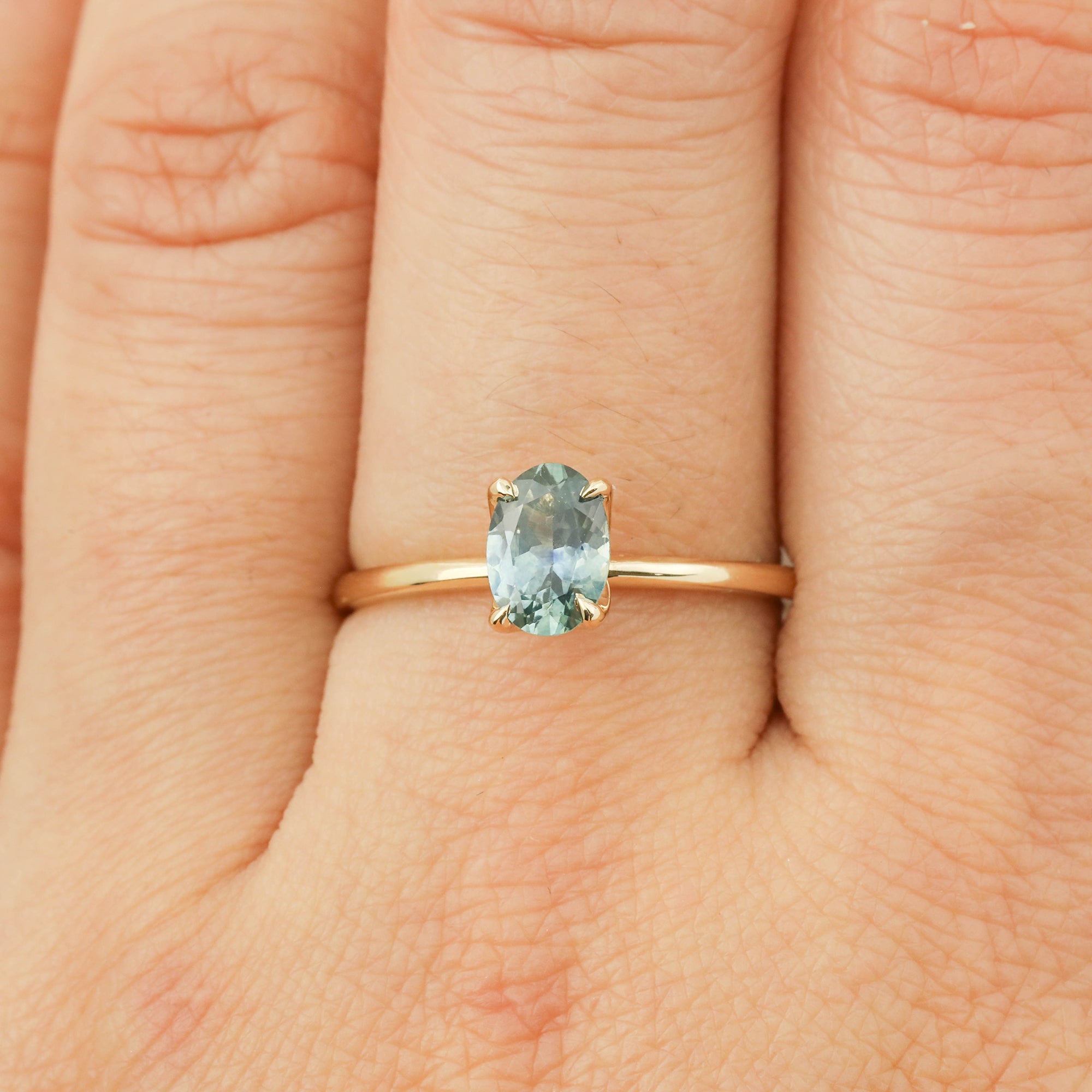 Elegant Sara Ring with 1.00ct parti blue green Montana sapphire set in 14k yellow gold band on finger.