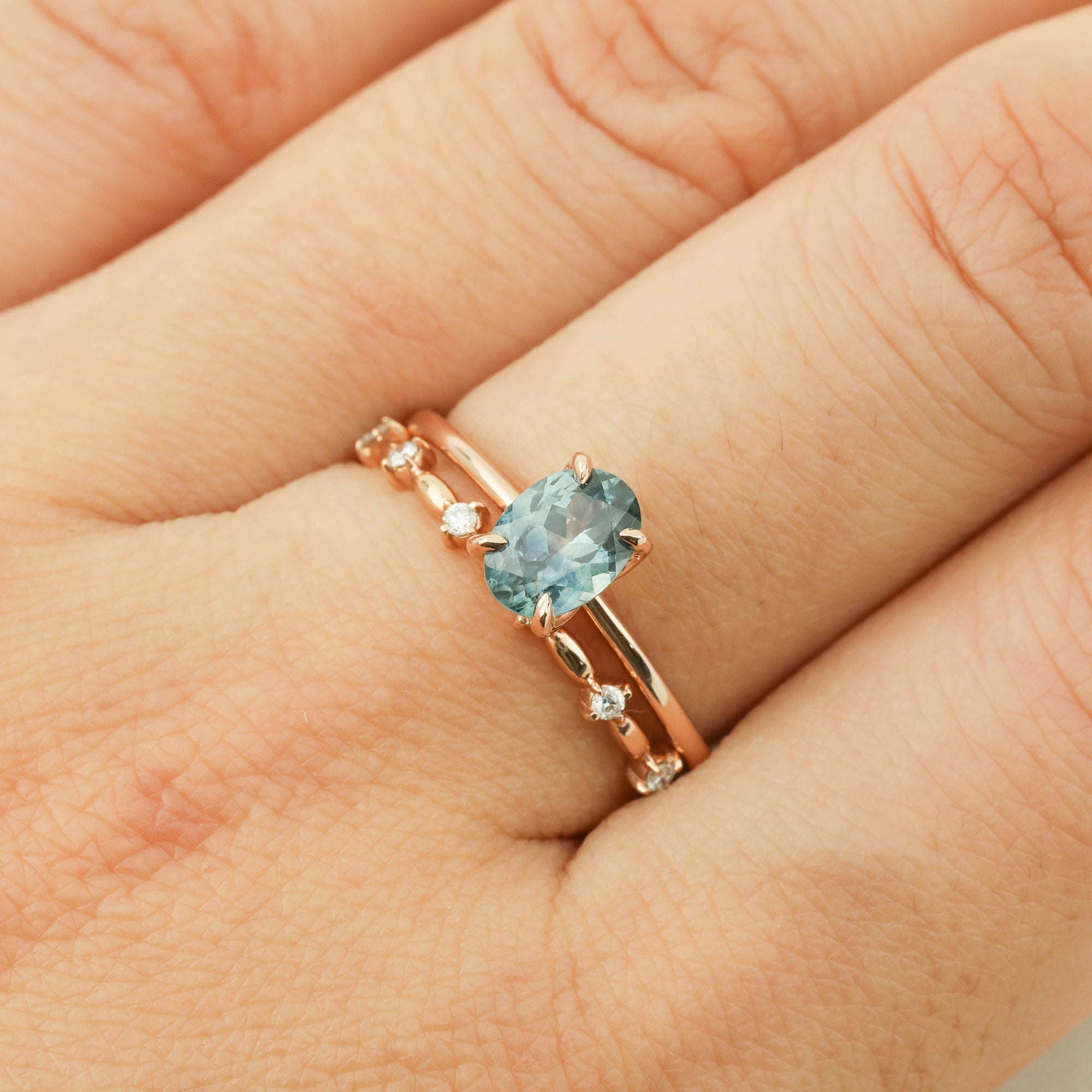 Close-up of hand wearing a 1.00ct teal blue Montana sapphire ring in 14k rose gold with accent diamonds