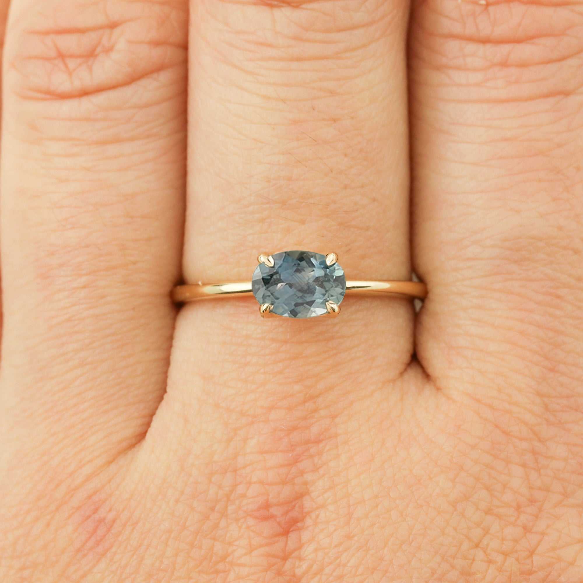 14k yellow gold ring with 1.12ct light blue-green Montana sapphire in classic four-prong setting on finger.
