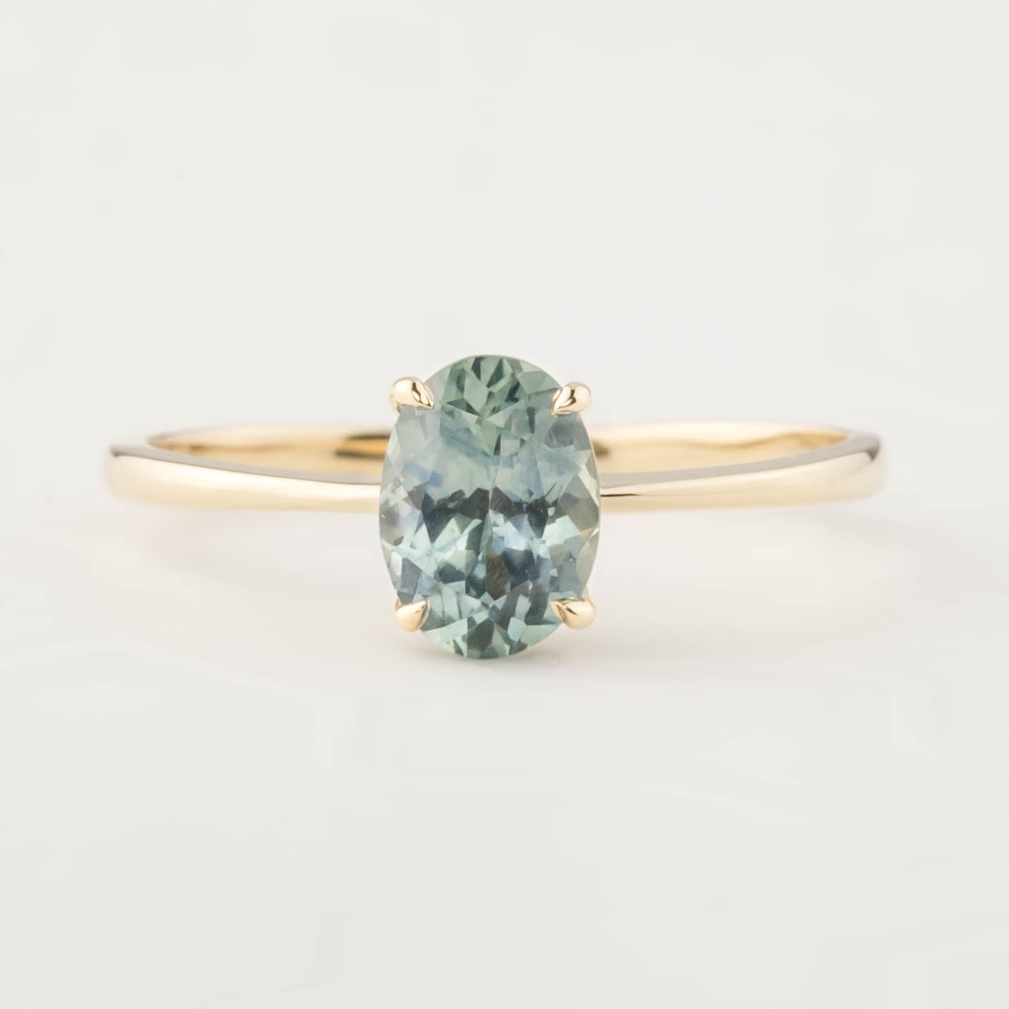 Oval light teal blue Montana sapphire ring set in 14k yellow gold with a delicate tapered band in classic four-prong setting