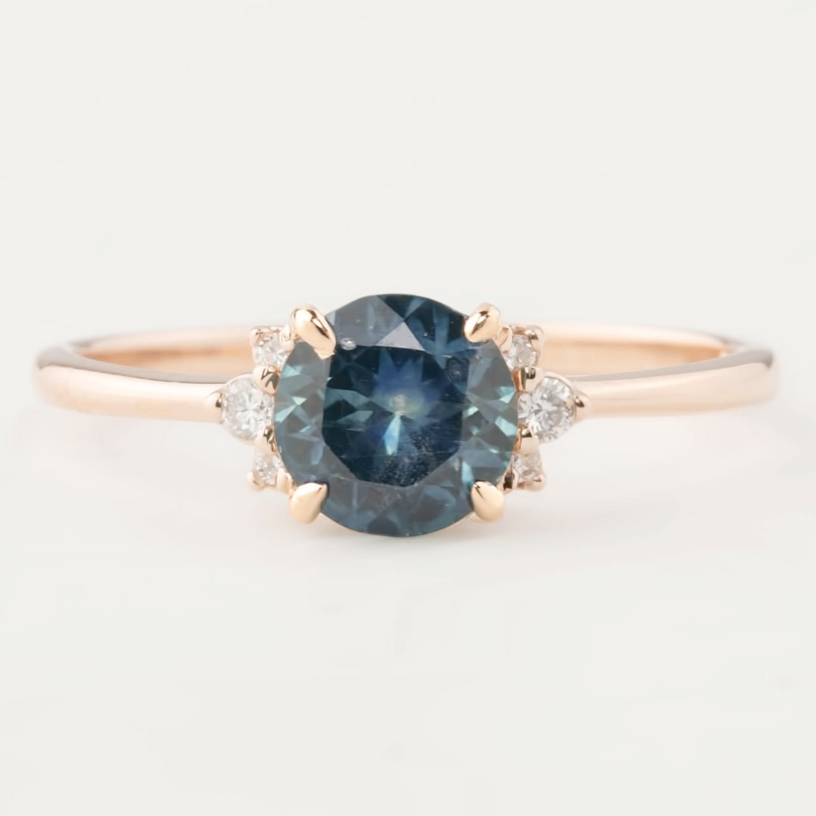 Rose gold ring with a 1.15ct teal blue Montana sapphire and small white diamond accents in a four-prong setting.
