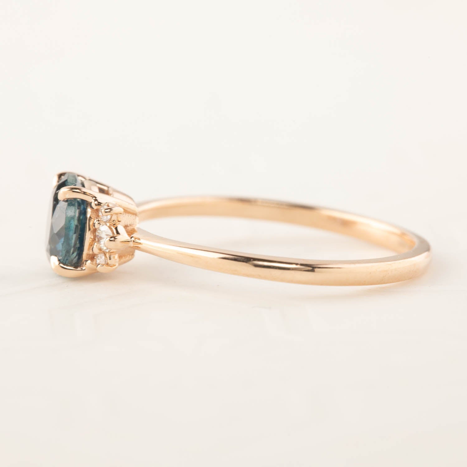 Side view of Lena ring with 1.15ct teal blue Montana sapphire and 14k rose gold band, classic low-profile setting.