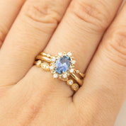 Close-up of a gold ring with an oval blue sapphire surrounded by small white diamonds on a finger