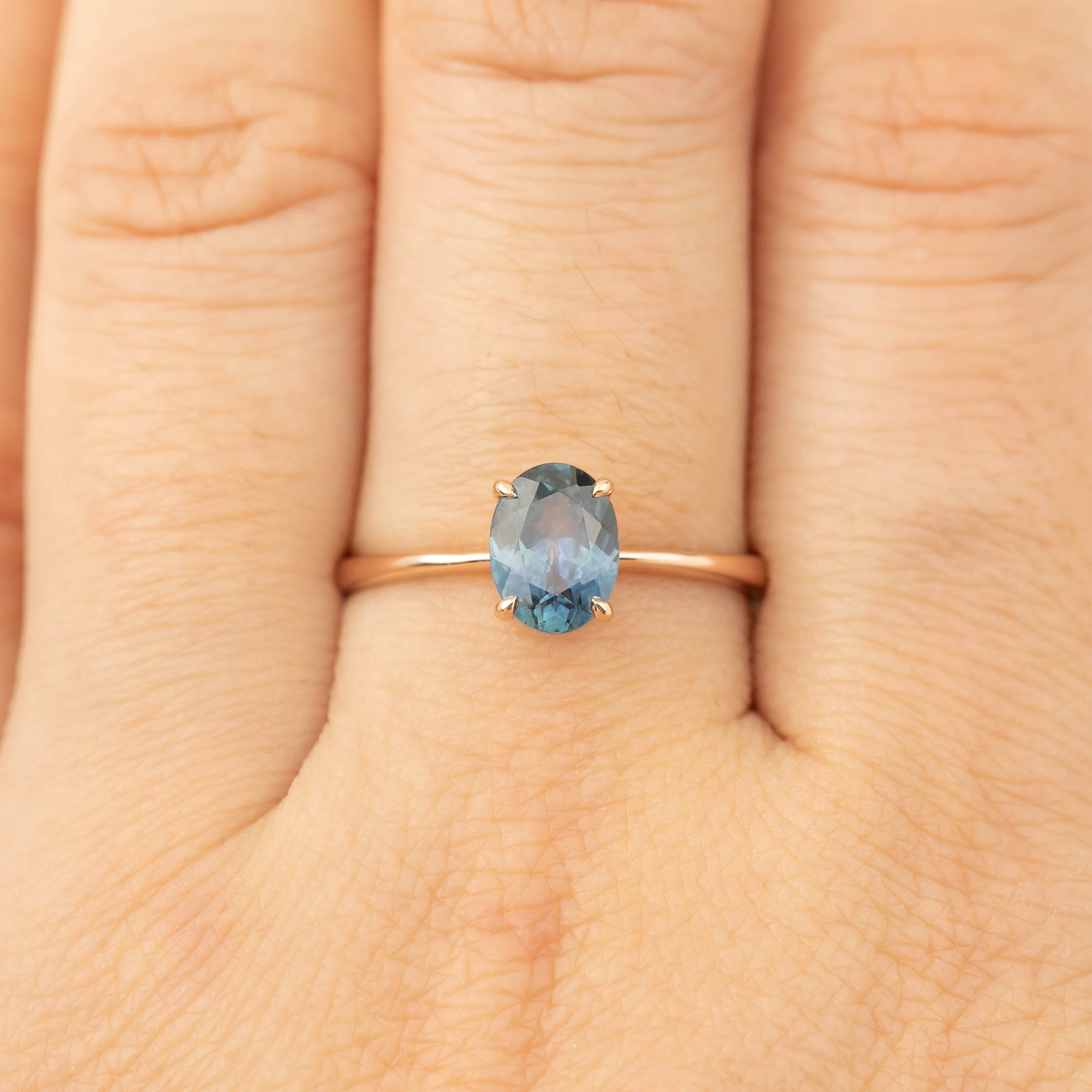 Close-up of Nina Ring with 1.24ct teal blue Montana sapphire in 14k rose gold on a finger size US7