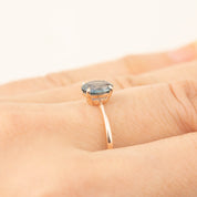Close-up of Nina Ring with 1.24ct teal blue Montana sapphire set in 14k rose gold on finger, low profile classic prong design.