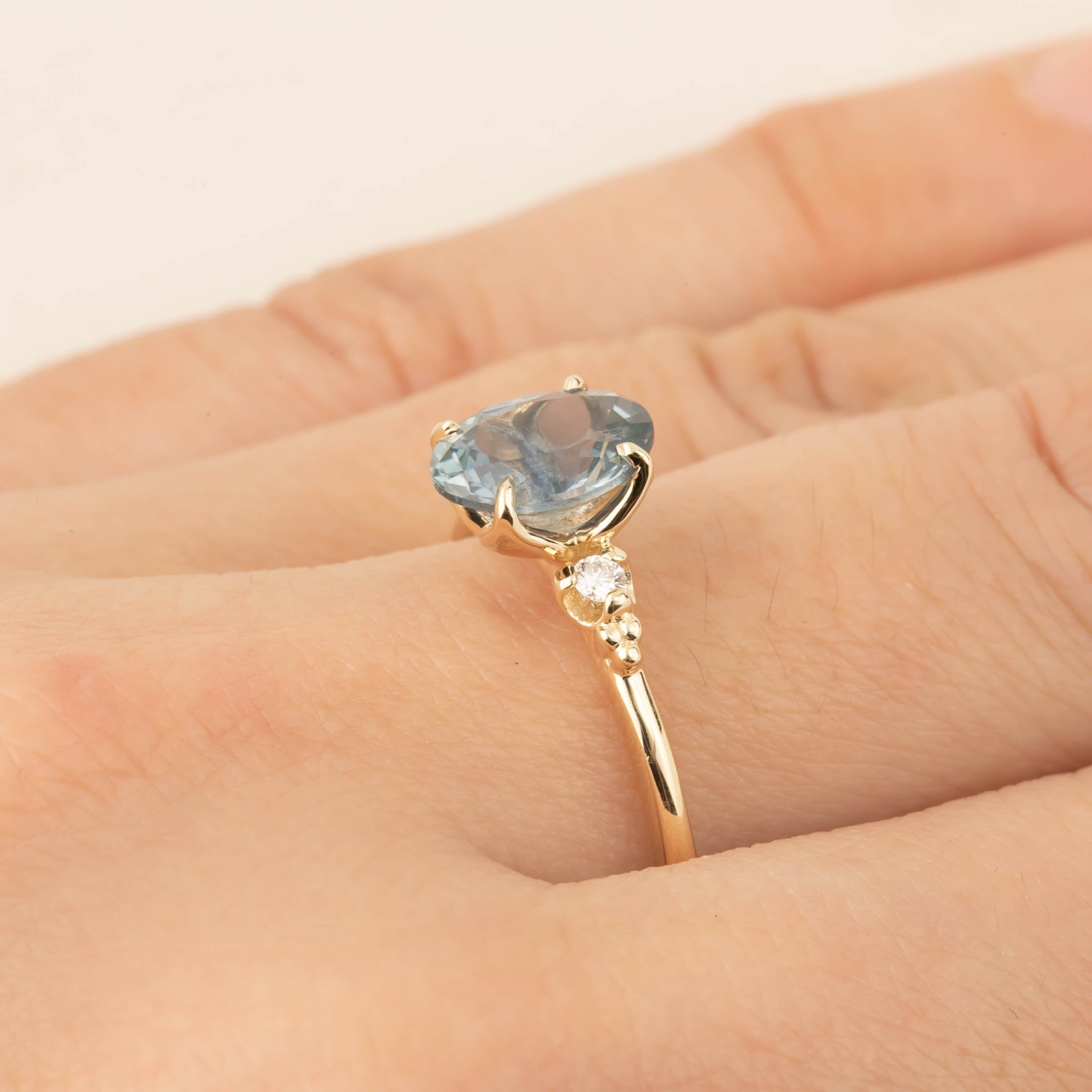 Gold ring with 1.62ct teal Montana sapphire and small white diamond accent worn on finger, size 7 adjustable band.