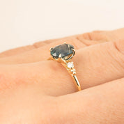 Close-up of a 14k gold ring with a 1.56ct teal blue Montana sapphire and small white accent diamonds on finger