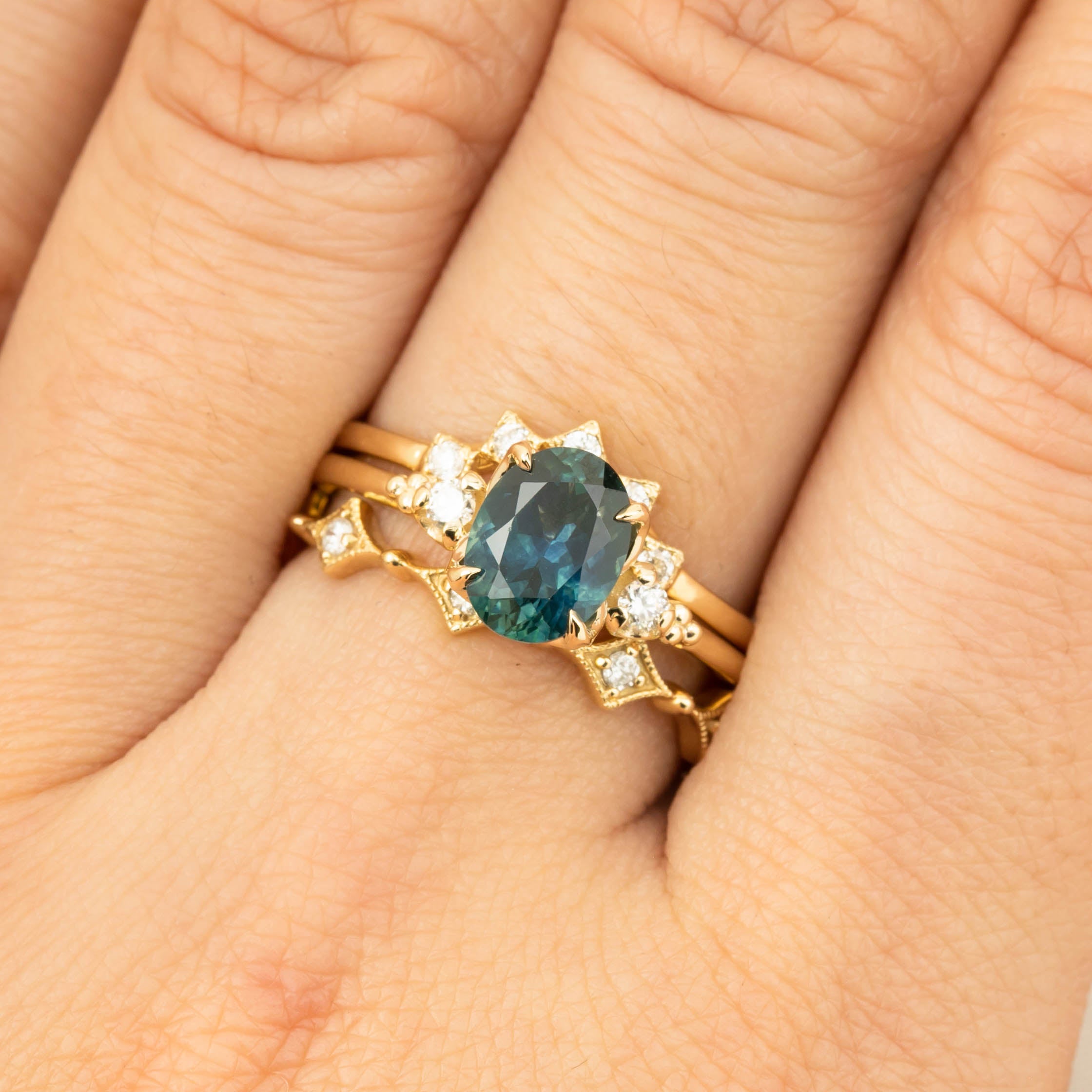 Close-up of a hand wearing a one-of-a-kind 1.56ct teal blue Montana sapphire ring with white diamonds in 14k gold