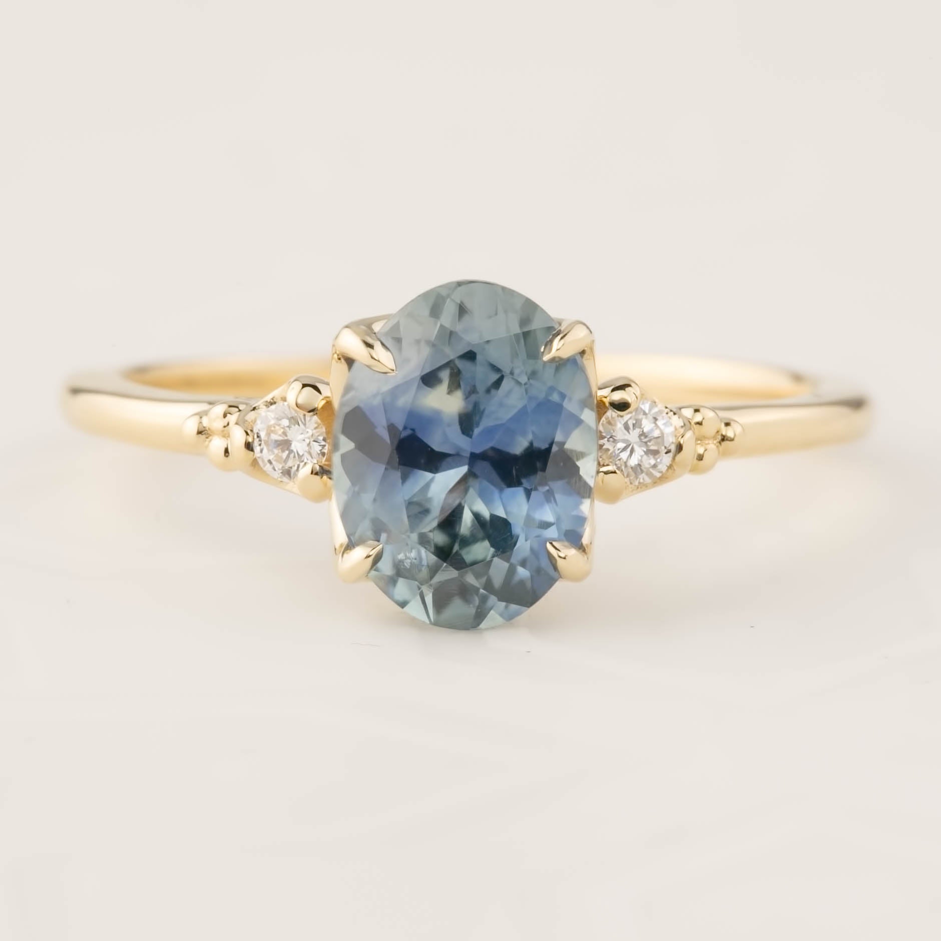 Gold ring featuring a 1.62ct teal Montana sapphire and two small white diamond accents in a four-prong setting.