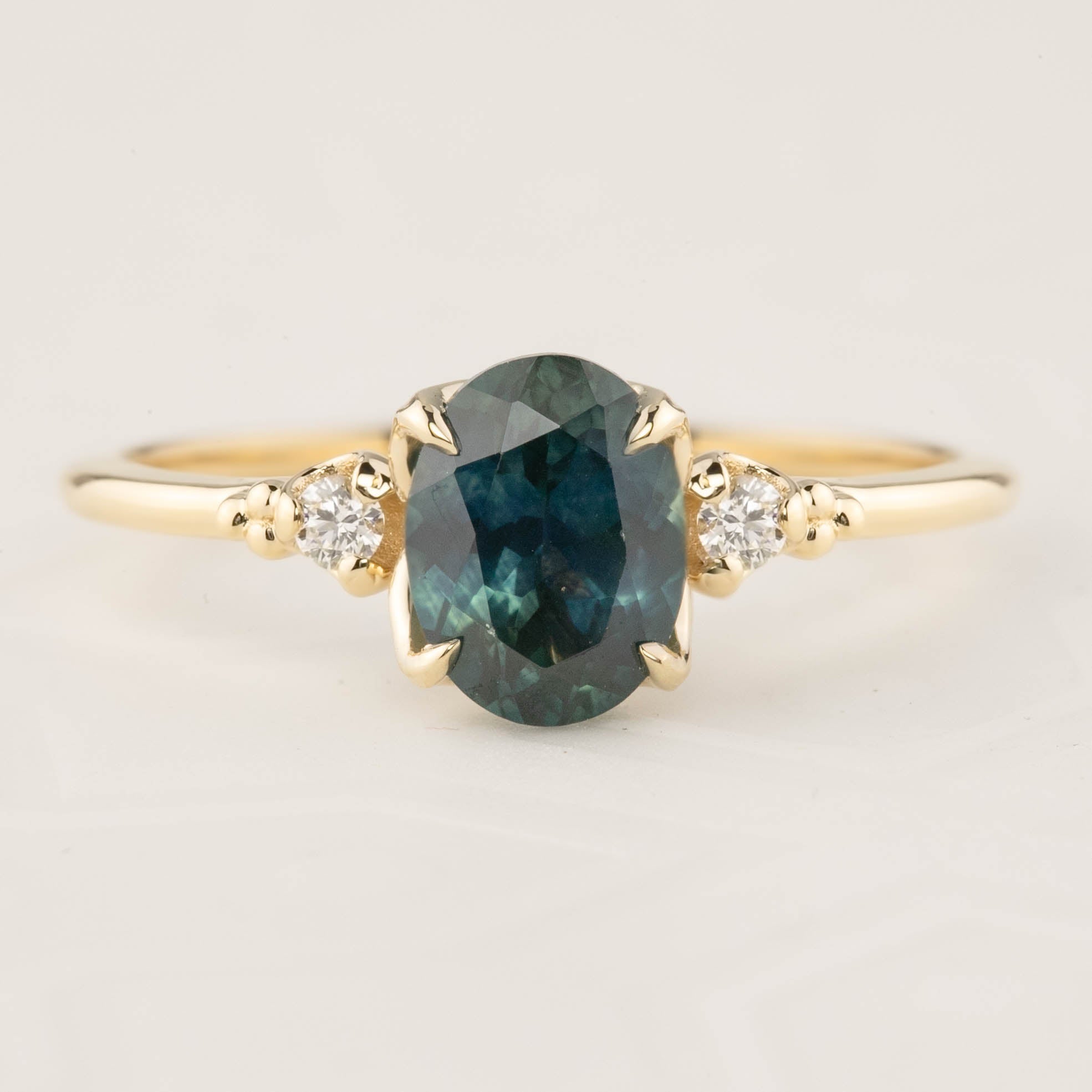 14k gold ring with 1.56ct teal blue Montana sapphire and two white accent diamonds in flower setting
