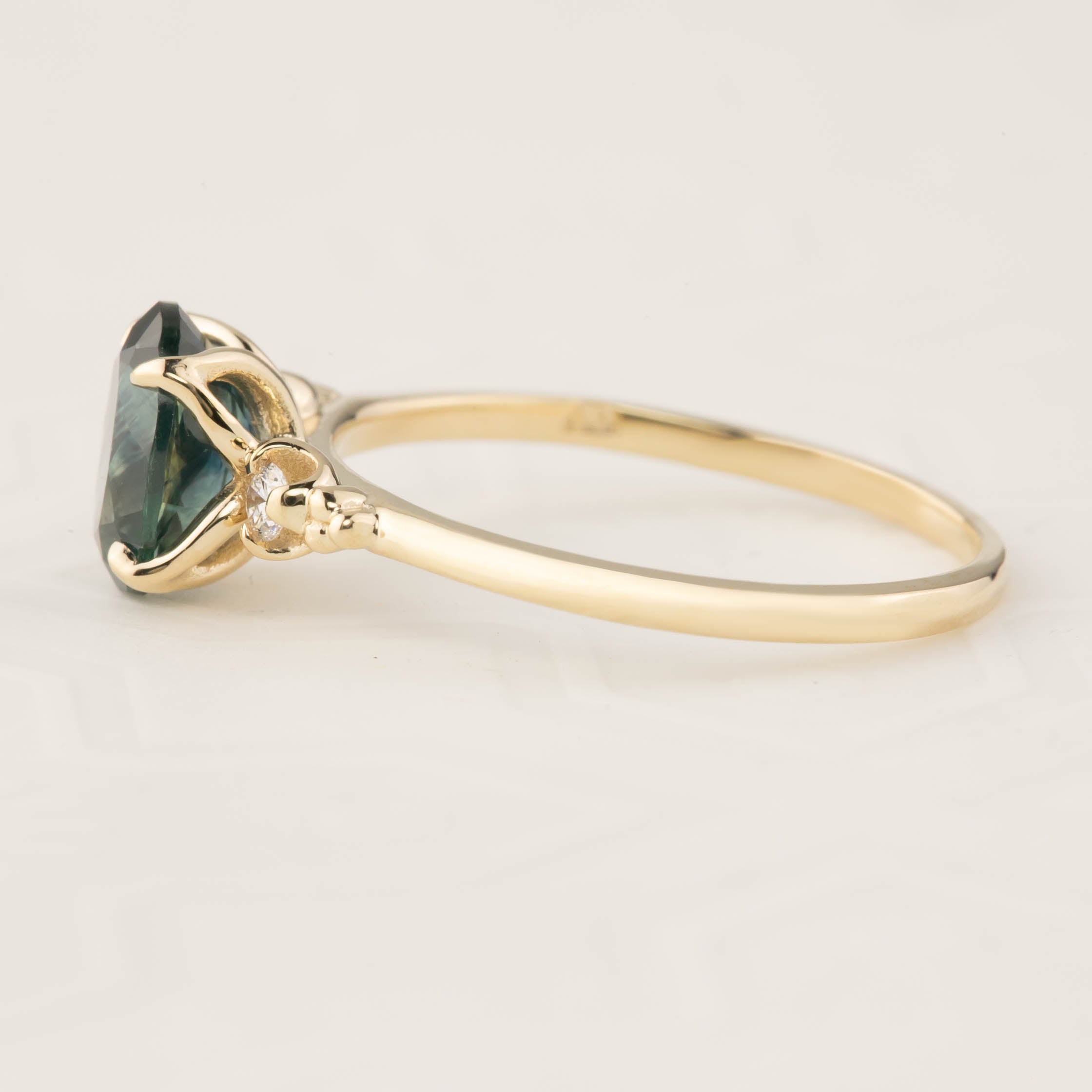 Side view of Estel Ring with 1.56ct teal blue Montana sapphire set in recycled 14k gold band with diamond accents