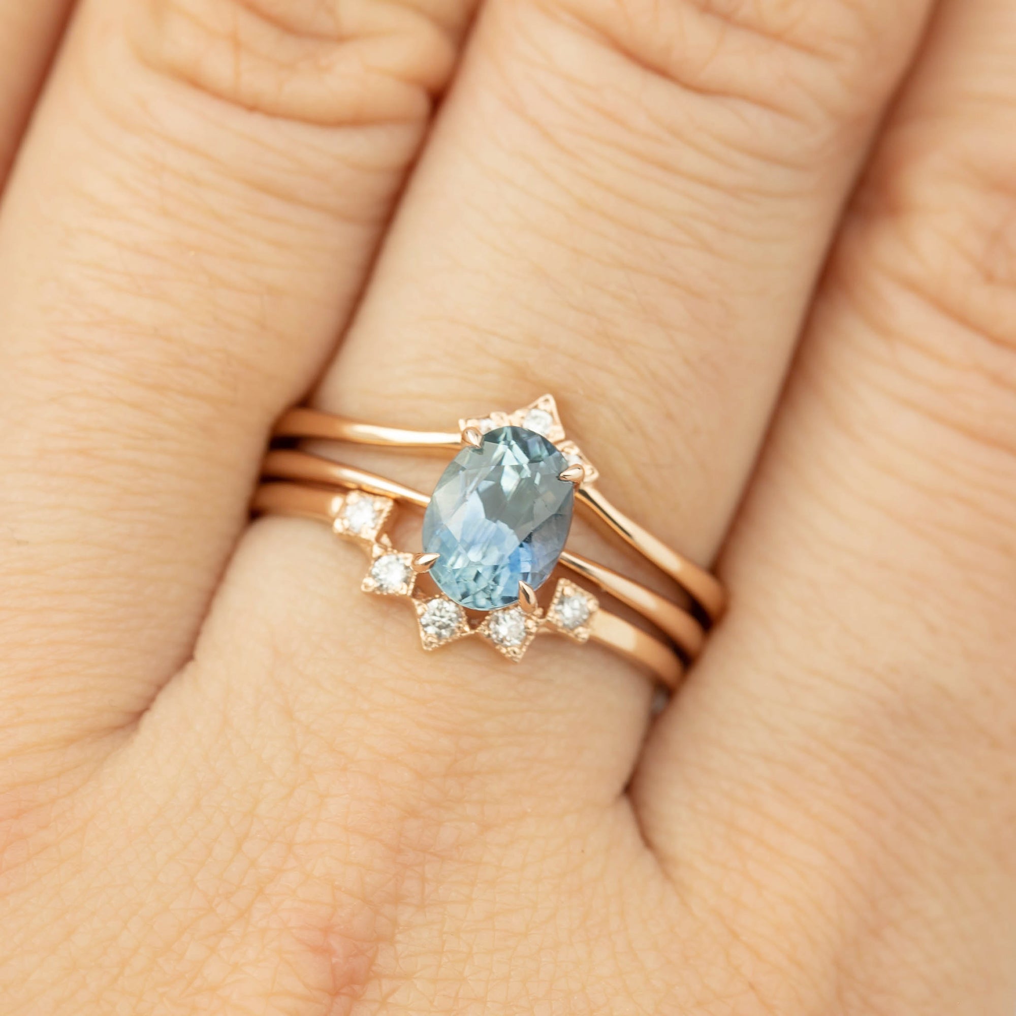 Close-up of a 1.4ct blue Montana sapphire ring set in recycled 14k rose gold with diamond accents on a hand.